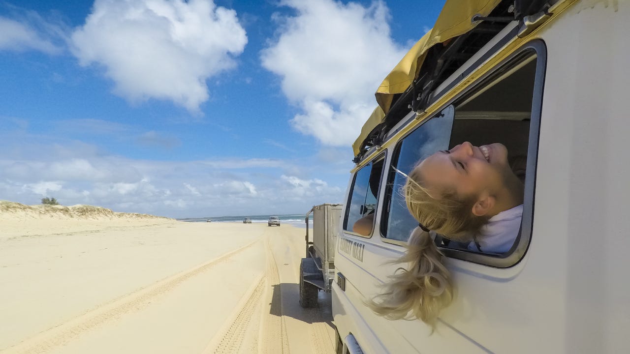 A woman sticks her head out the window of a jeep and enjoys the breeze during a road trip.