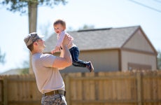 Young male soldier holding up toddler daughter in garden at air force military base