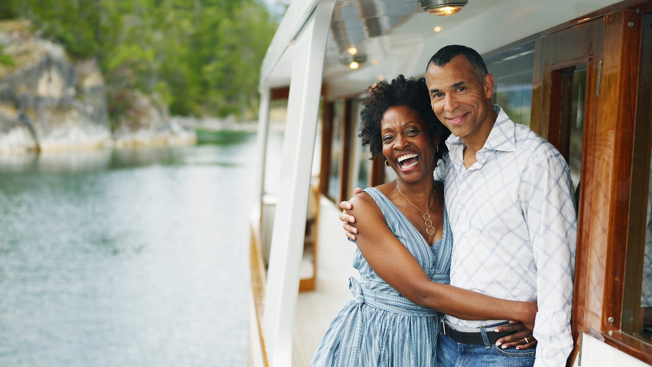 An older Black couple hangs off a boat
