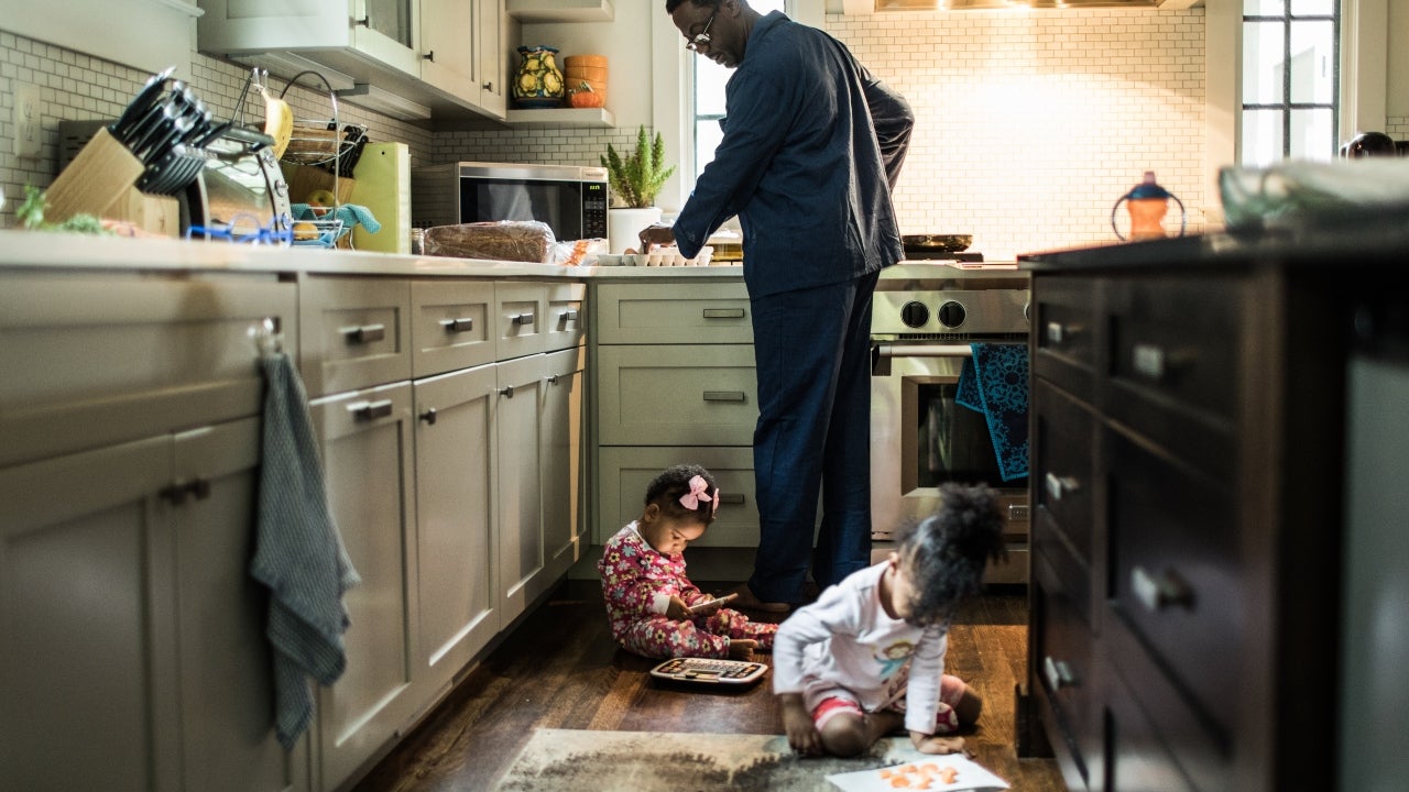 A father makes breakfast for his two young children at home.