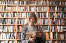 An old white woman flips through a book in front of a bookshelf