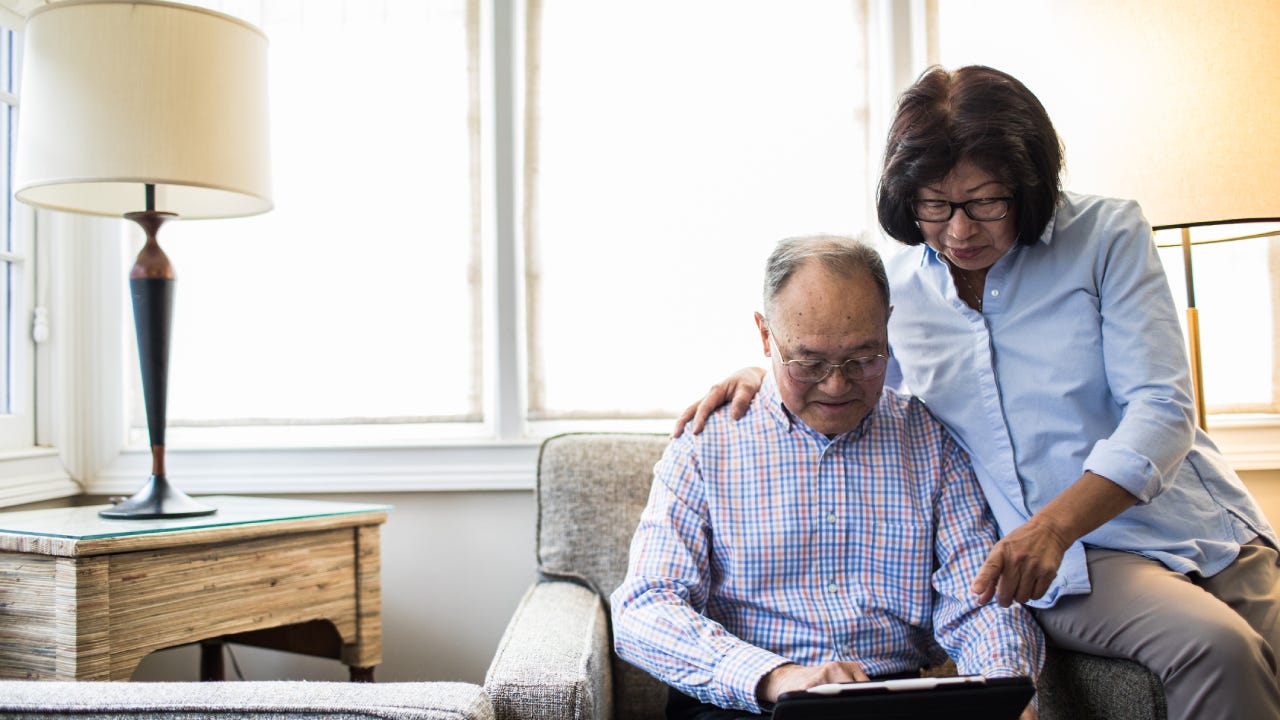 An older Asian couple sitting in their living room on a laptop, reviewing their finances.