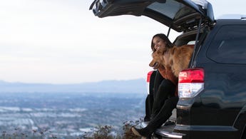 Young woman sitting in the back of her car with her golden retriever