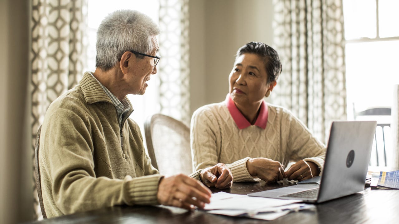 An older Asian couple sits down at the kitchen table to look at their insurance documents.
