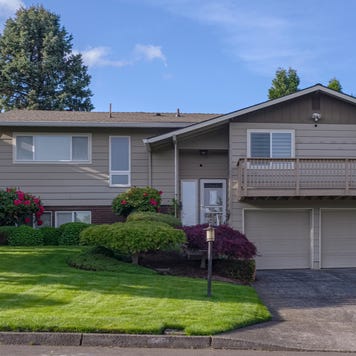 The exterior of a beige split-level home with garage, driveway and yard