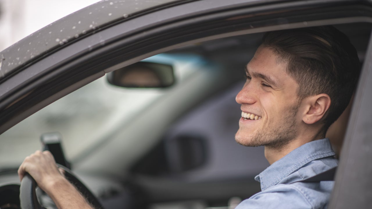 A young man in the driver's seat of his car smiling and enjoying life.