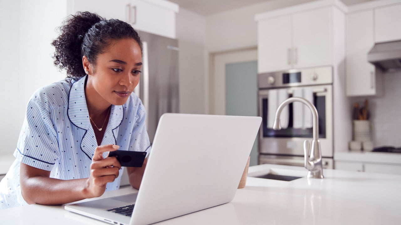 Woman holding card while looking at laptop.