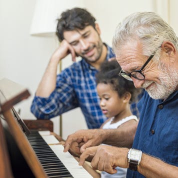 An old man sits with his son and granddaughter and plays on the piano.