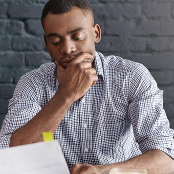 Young man with ponderous expression reviewing paperwork