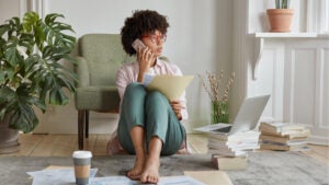 Young woman sitting on living room floor organizing finances on phone