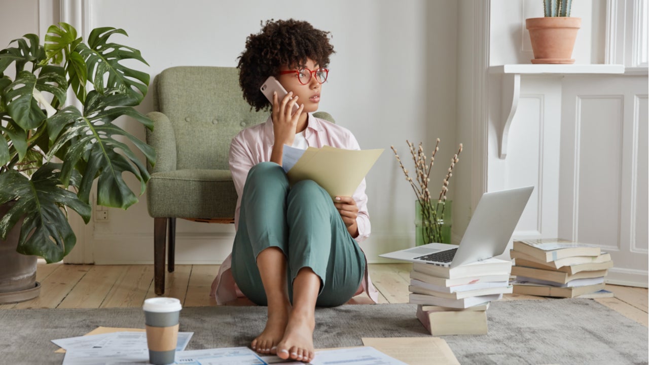 Young woman sitting on living room floor organizing finances on phone