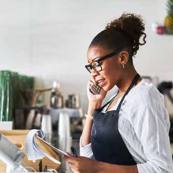 friendly waitress taking order on phone at restaurant and writing on notepad