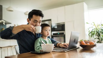 A father sits with his son in front of the laptop while sipping his coffee.