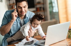 Father working from home while holding baby daughter