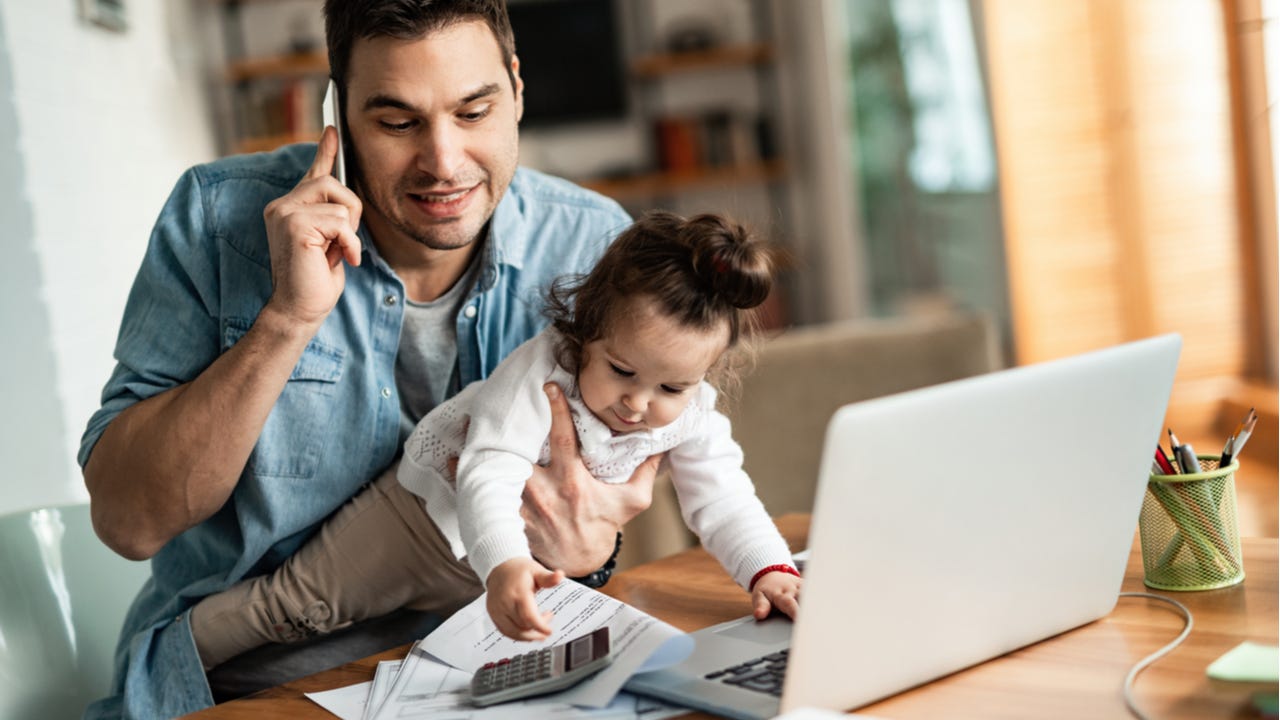 Father working from home while holding baby daughter