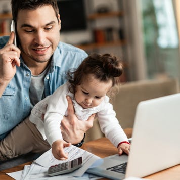 Father working from home while holding baby daughter