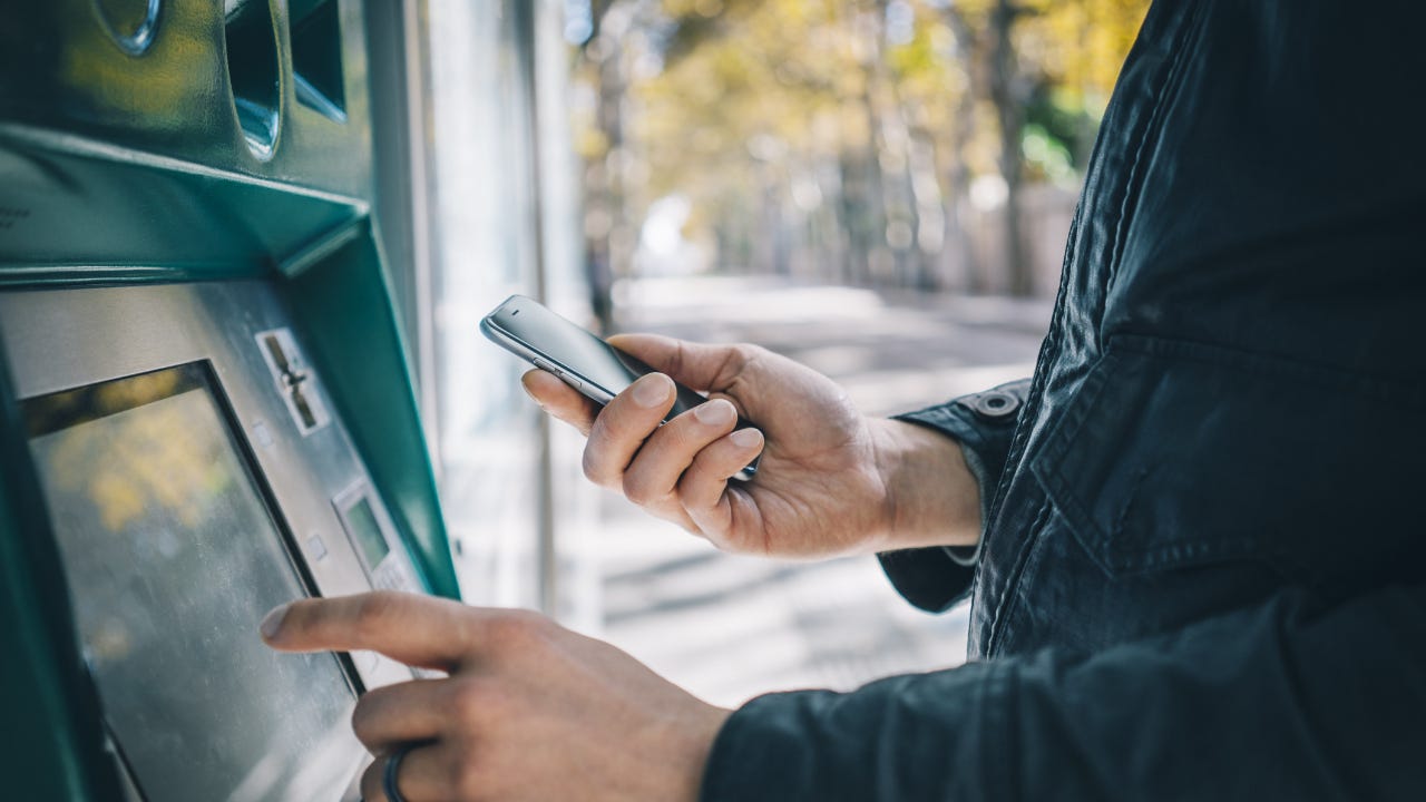 A man uses his phone at an ATM.