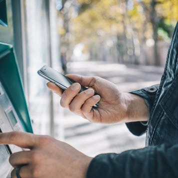 A man uses his phone at an ATM.