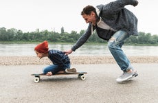 A father pushes his son along on a skateboard