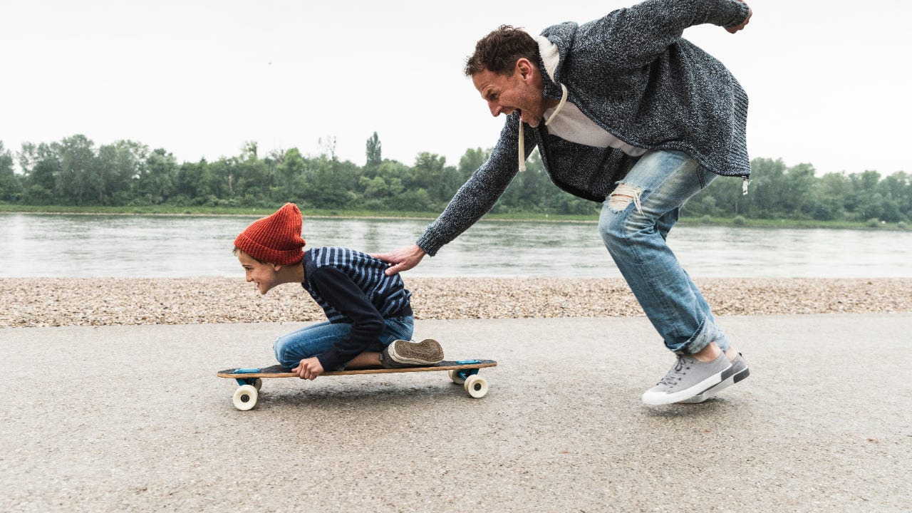 A father pushes his son along on a skateboard