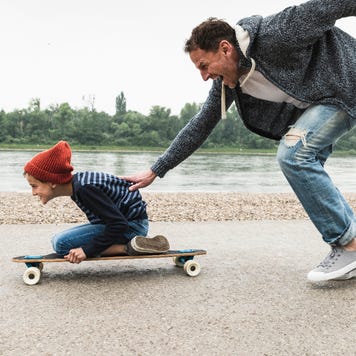 A father pushes his son along on a skateboard