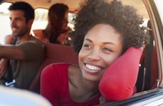 Black woman sits on passenger side of car with her face and arm out the window, enjoying the breeze.