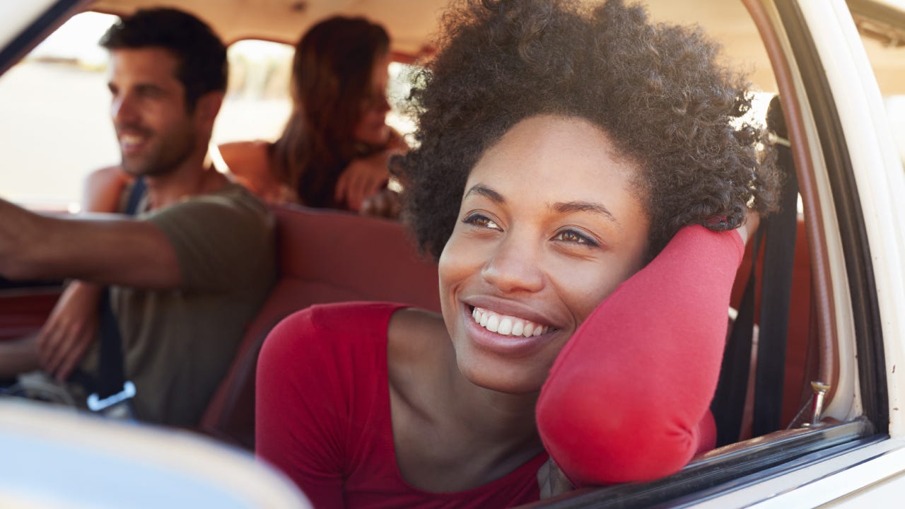 Black woman sits on passenger side of car with her face and arm out the window, enjoying the breeze.