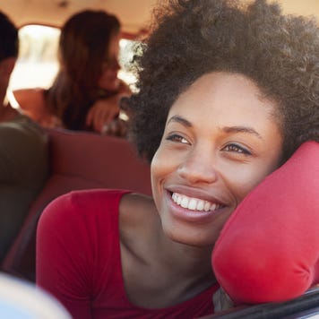 Black woman sits on passenger side of car with her face and arm out the window, enjoying the breeze.