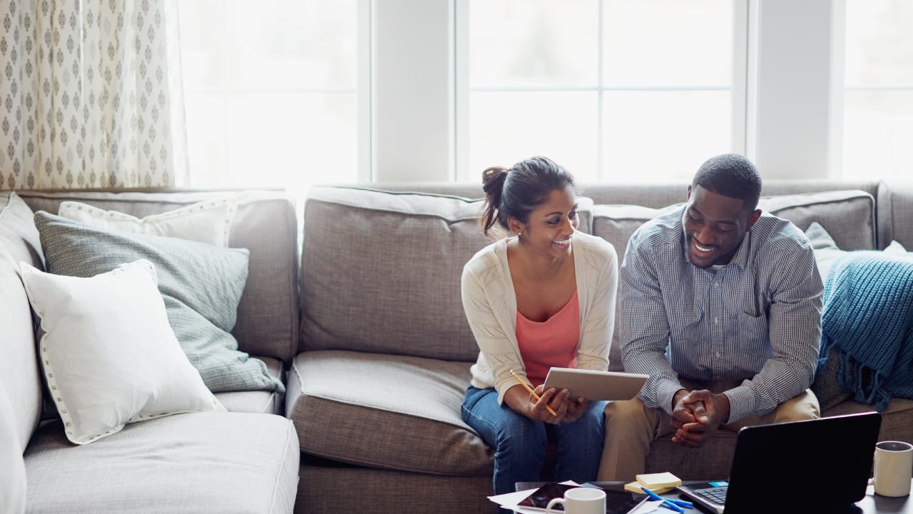 A couple sits together on the couch in a living room going over their finances.