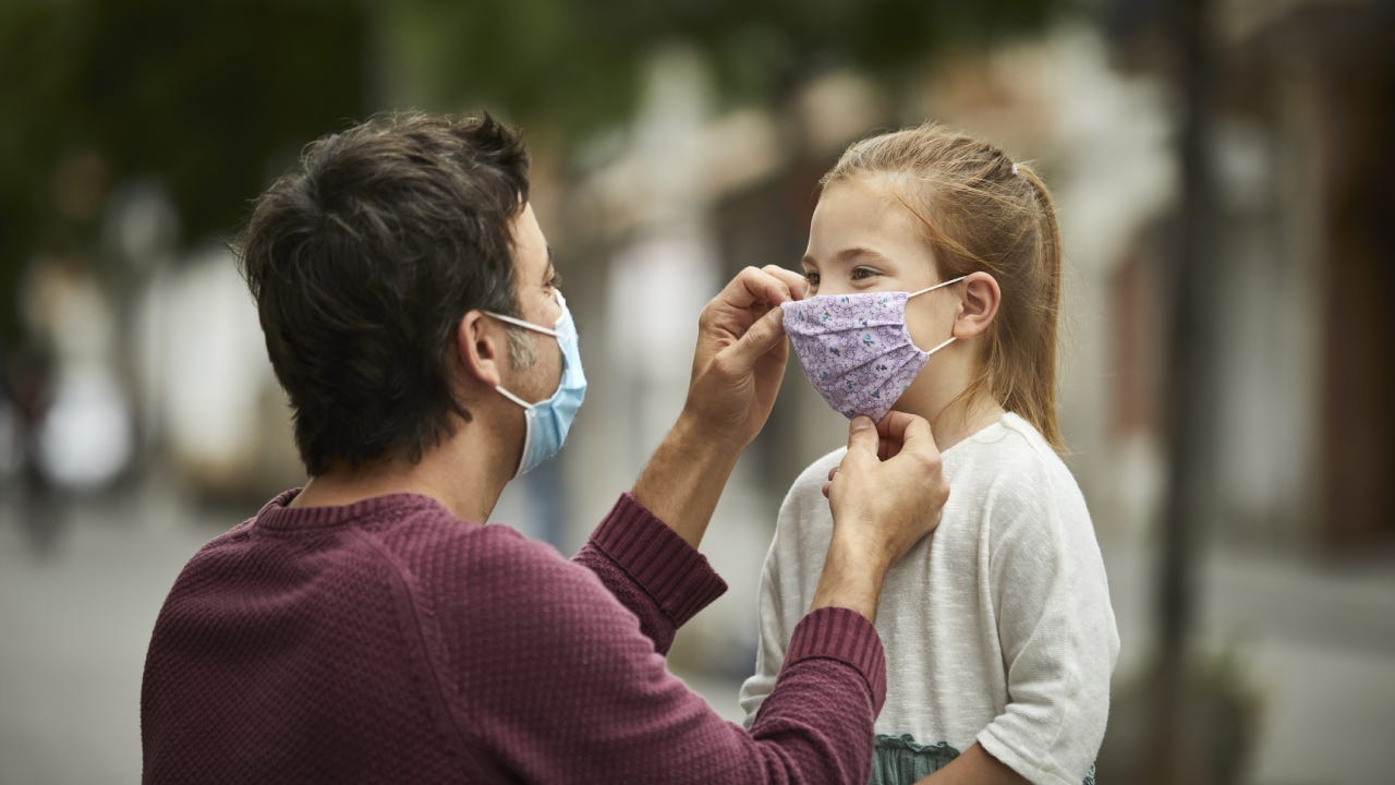 A father helps put a mask on his daughter to protect against COVID-19.