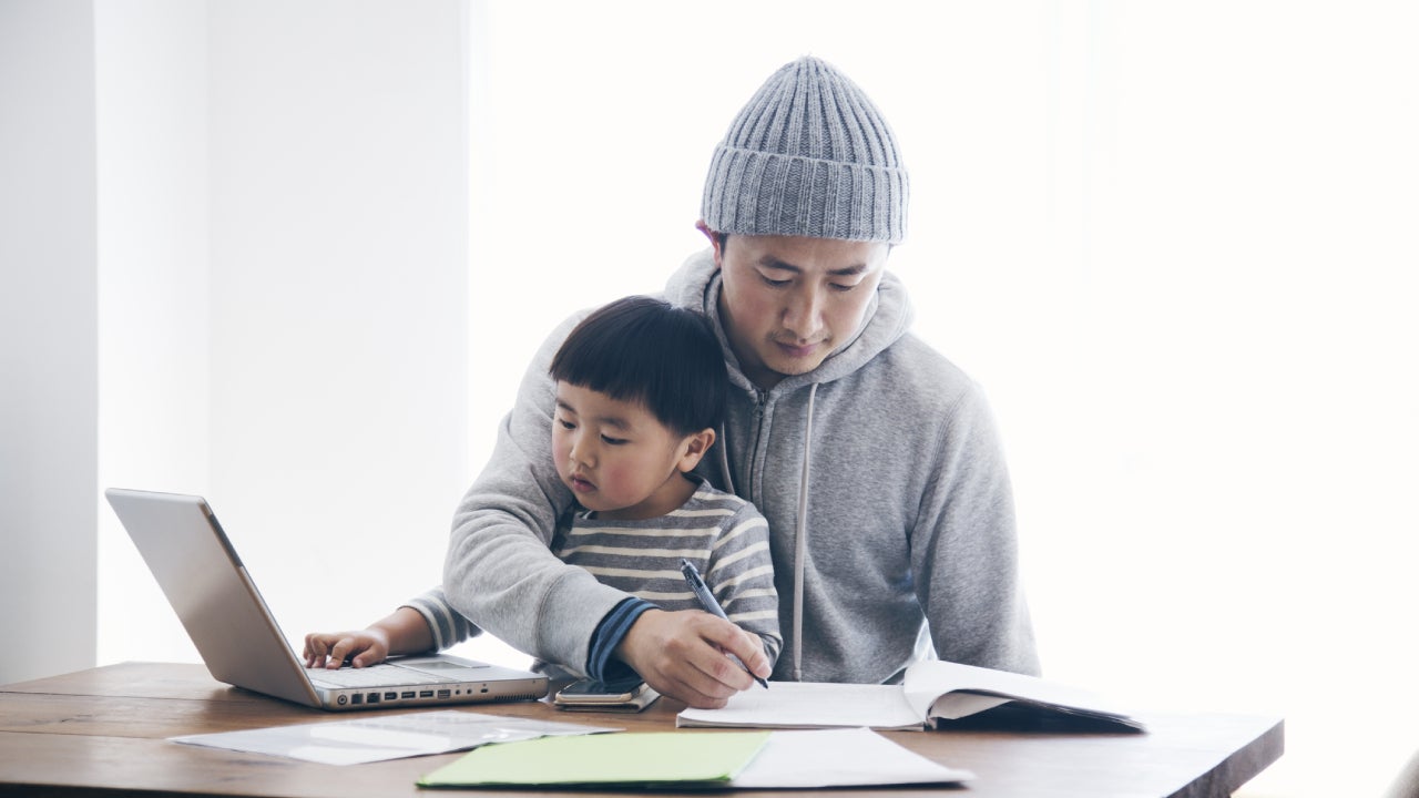 Asian father sits with his young son on his lap in the kitchen, working out his bills and finances.