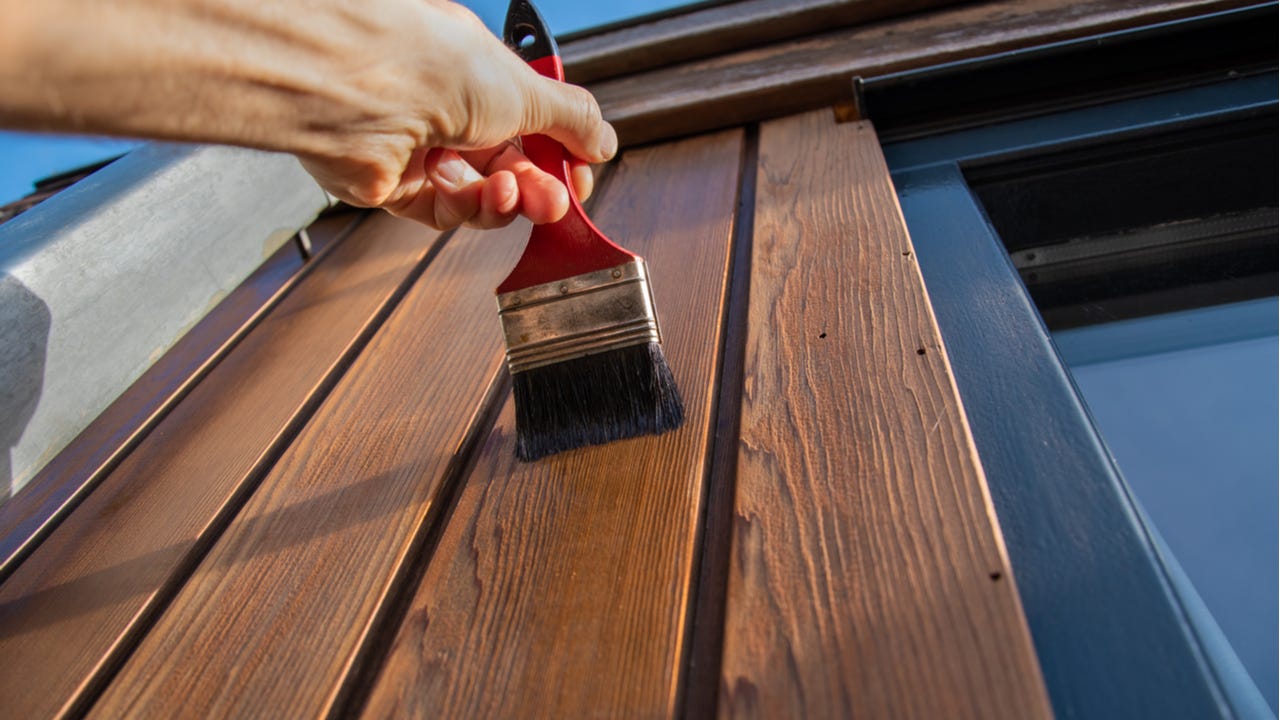 A closeup of a painter painting the exterior of a home