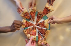 seven hands each take a slice of pizza from the same pie