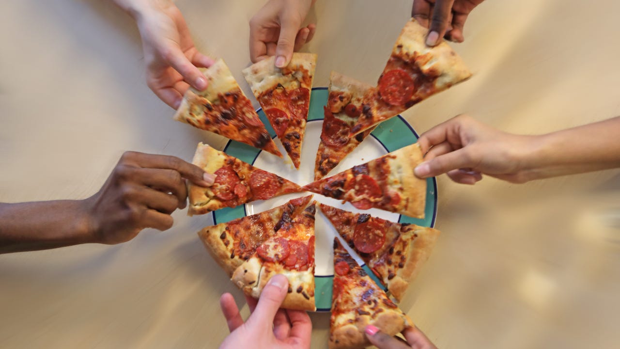 seven hands each take a slice of pizza from the same pie