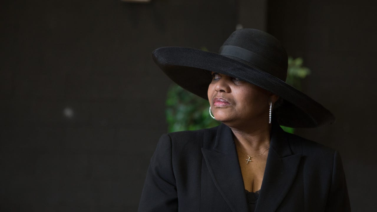 A black woman in a black dress and hat at a funeral.