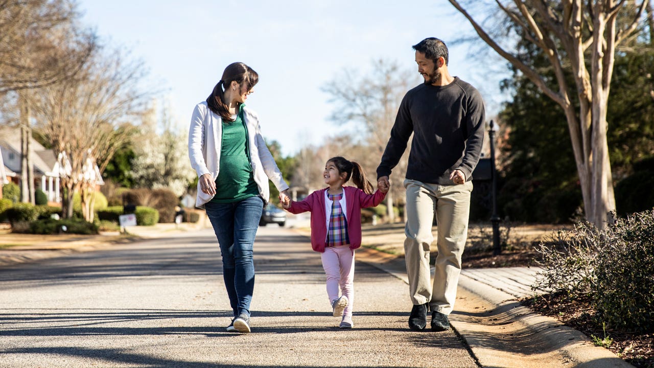 parents and young daughter walking on street together in suburban neighborhood