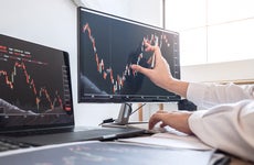 A man's hand traces a stock chart on a computer monitor