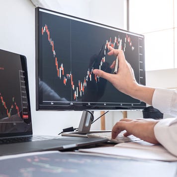 A man's hand traces a stock chart on a computer monitor