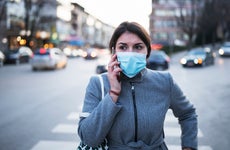 A women wearing a facemask talks on the phone while crossing the street