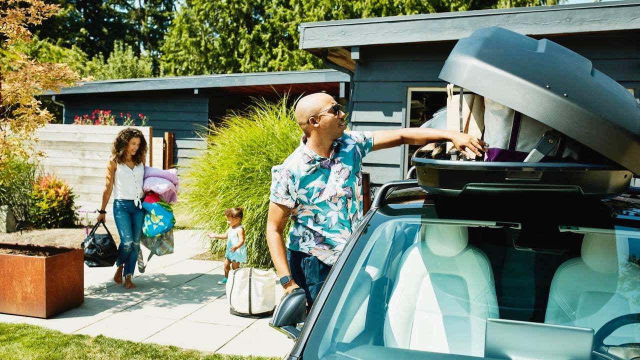 Family loading luggage into car top box before road trip