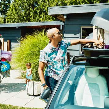 Family loading luggage into car top box before road trip