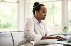 A black woman with her hair done up in a bun sitting at her desk in front of a laptop.