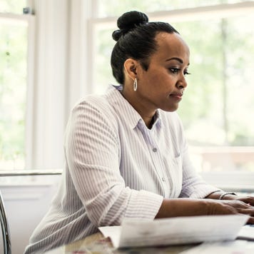 A black woman with her hair done up in a bun sitting at her desk in front of a laptop.