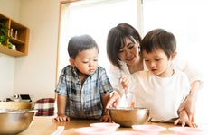 Asian single mother with her two children in the kitchen, showing them how to bake a cake.