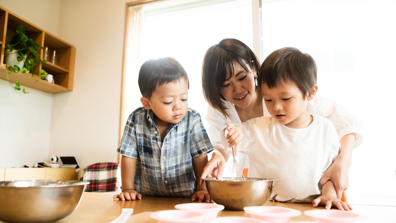 Asian single mother with her two children in the kitchen, showing them how to bake a cake.