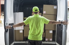 Working man in neon hat and shirt opens the rear doors to his delivery van revealing stacks of boxes for delivery.