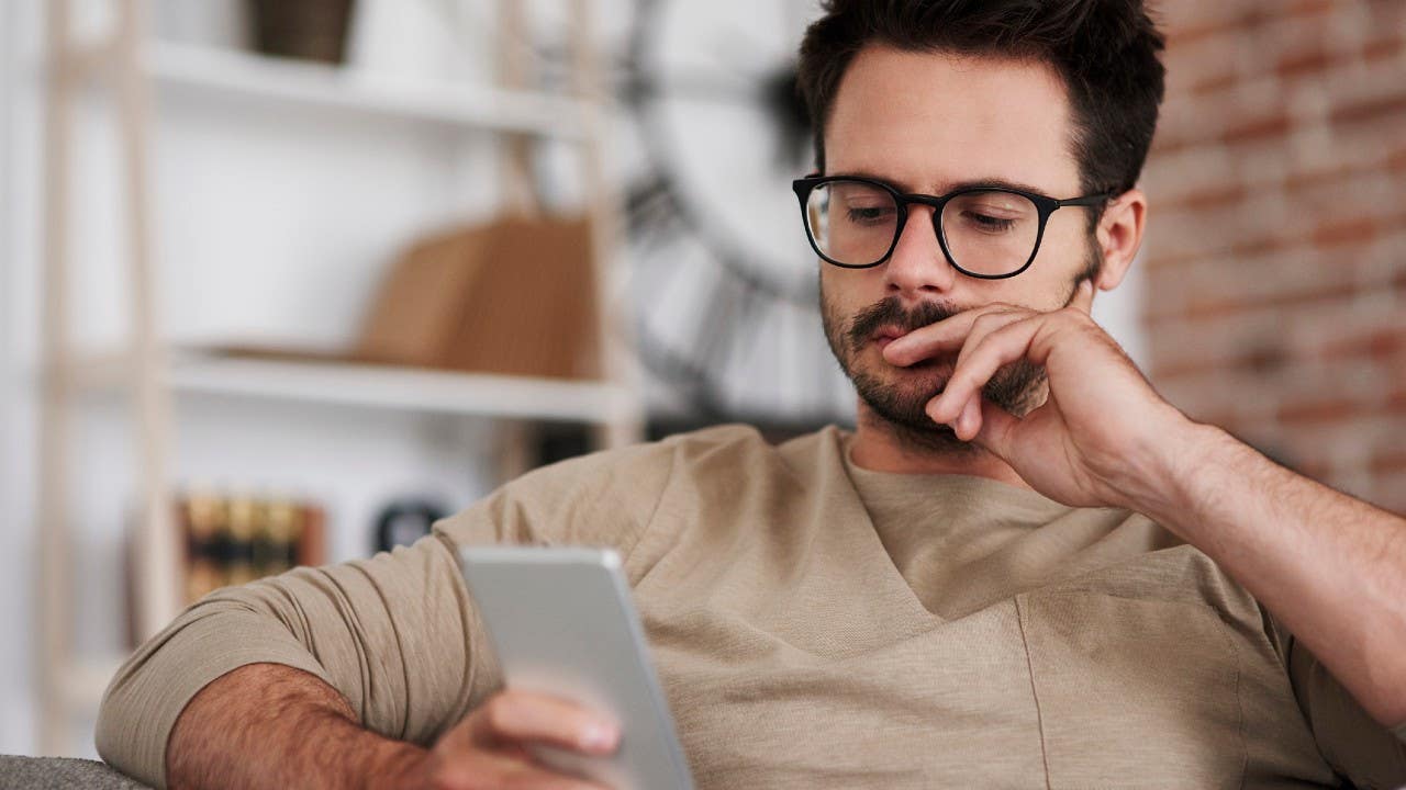 Man looks at cell phone, thinking