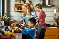 A same-sex couple does some cooking in the kitchen with their adopted Asian son.