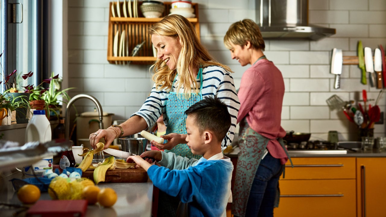 A same-sex couple does some cooking in the kitchen with their adopted Asian son.