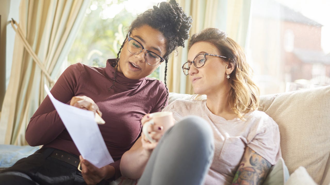 Same sex couple sits on the couch together reviewing their auto insurance policy.